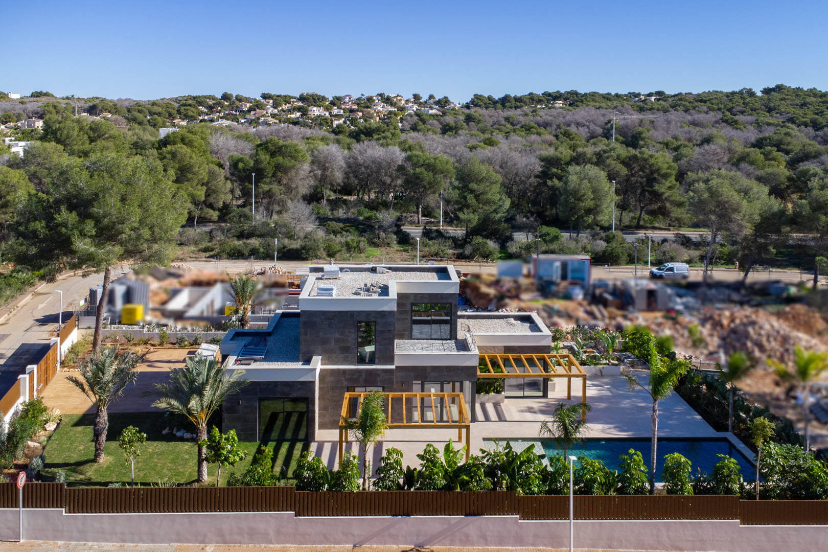 Vue aérienne de la villa moderne avec façade en pierre, pergolas en bois d'iroko, piscine de style Bali et jardin méditerranéen entouré de verdure.