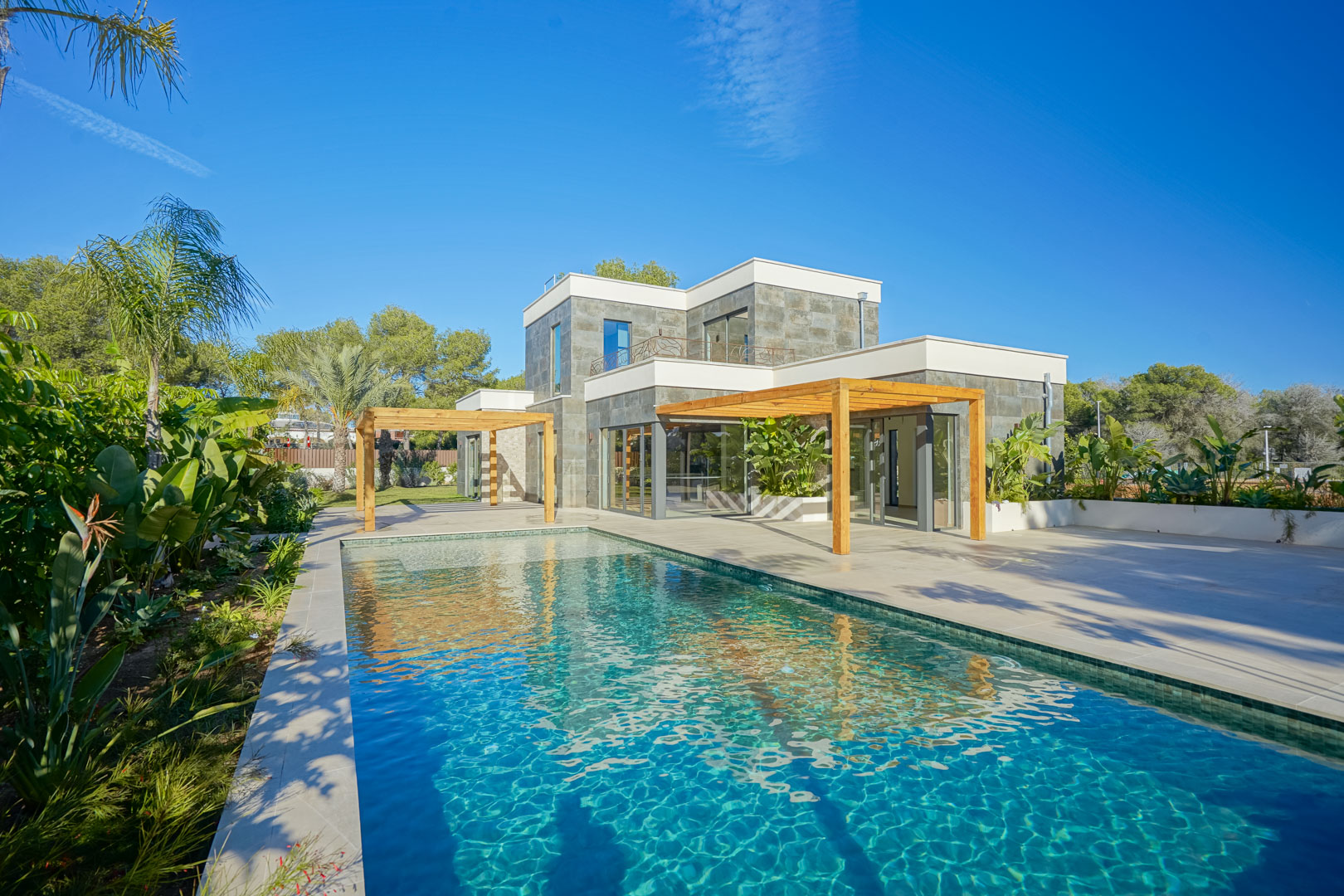 Vue extérieure de la villa avec piscine de style Bali, vastes terrasses et pergolas en bois d'iroko entourées d'un jardin méditerranéen.
