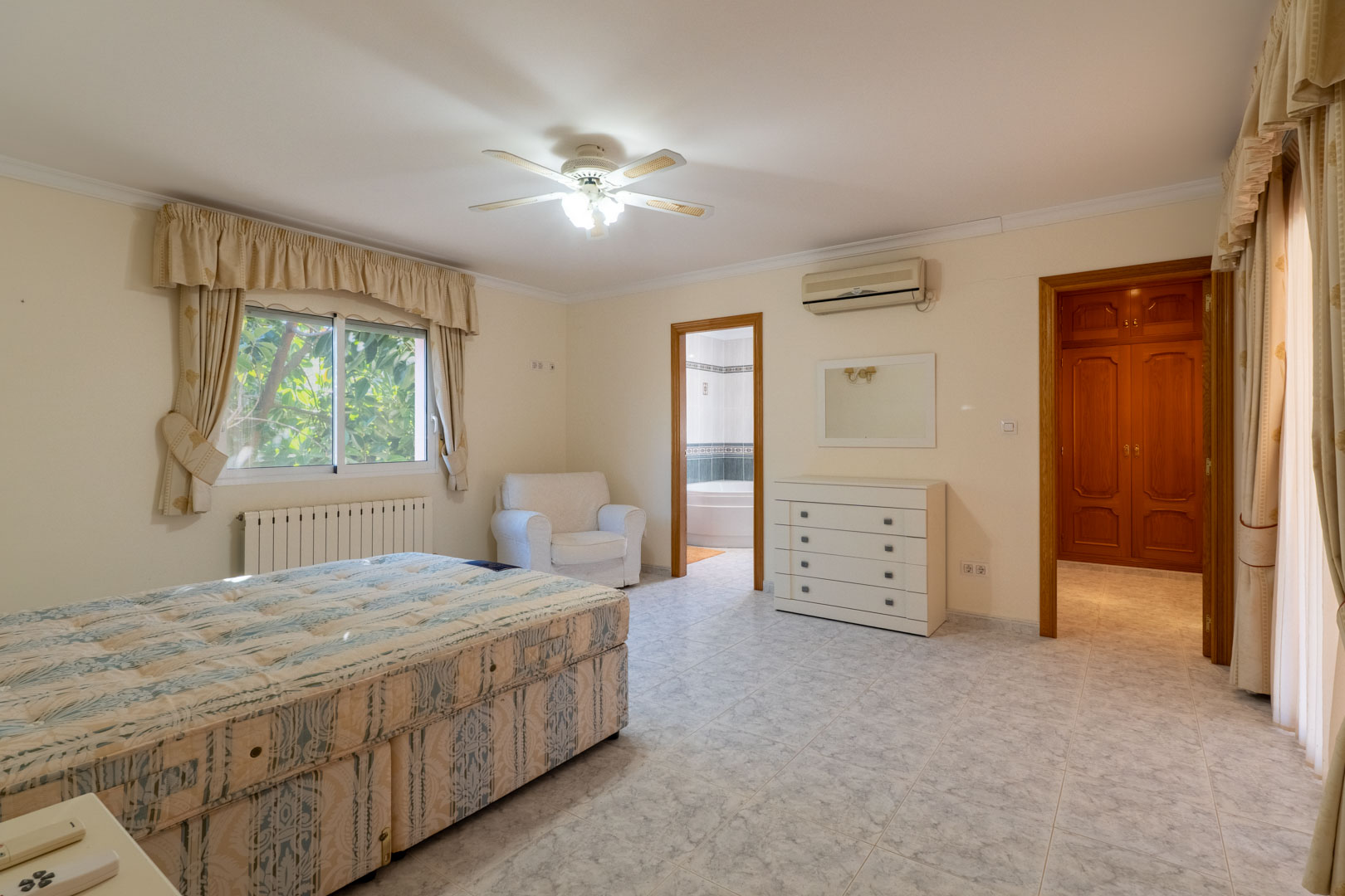 Chambre principale avec salle de bain attenante et dressing. Elle dispose de sols en céramique, d'une climatisation réversible, d'un ventilateur de plafond et de menuiseries en bois.