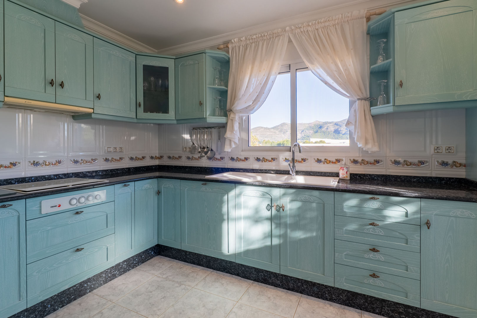 Cuisine indépendante avec meubles turquoise, plan de travail en granit noir et fenêtre offrant une vue dégagée sur les montagnes environnantes.