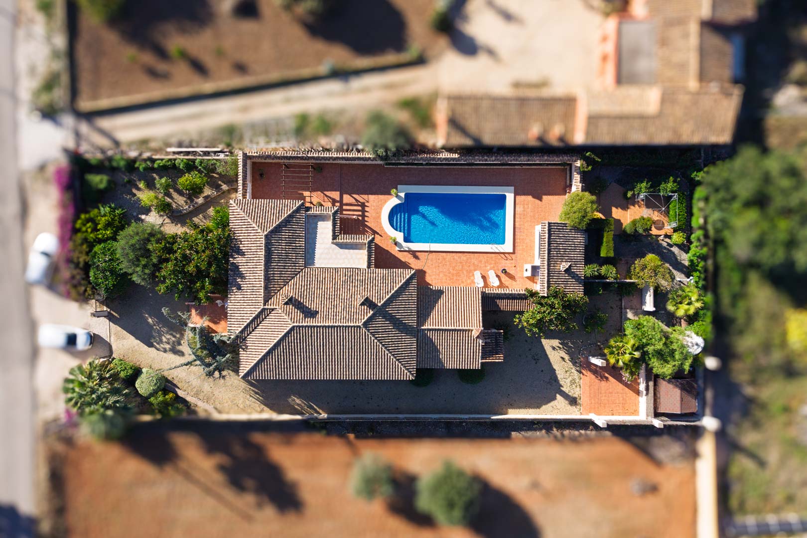 Vue aérienne zénithale de la villa sur un terrain plat, montrant la piscine rectangulaire, les vastes terrasses pavées et la toiture en tuiles romanes.