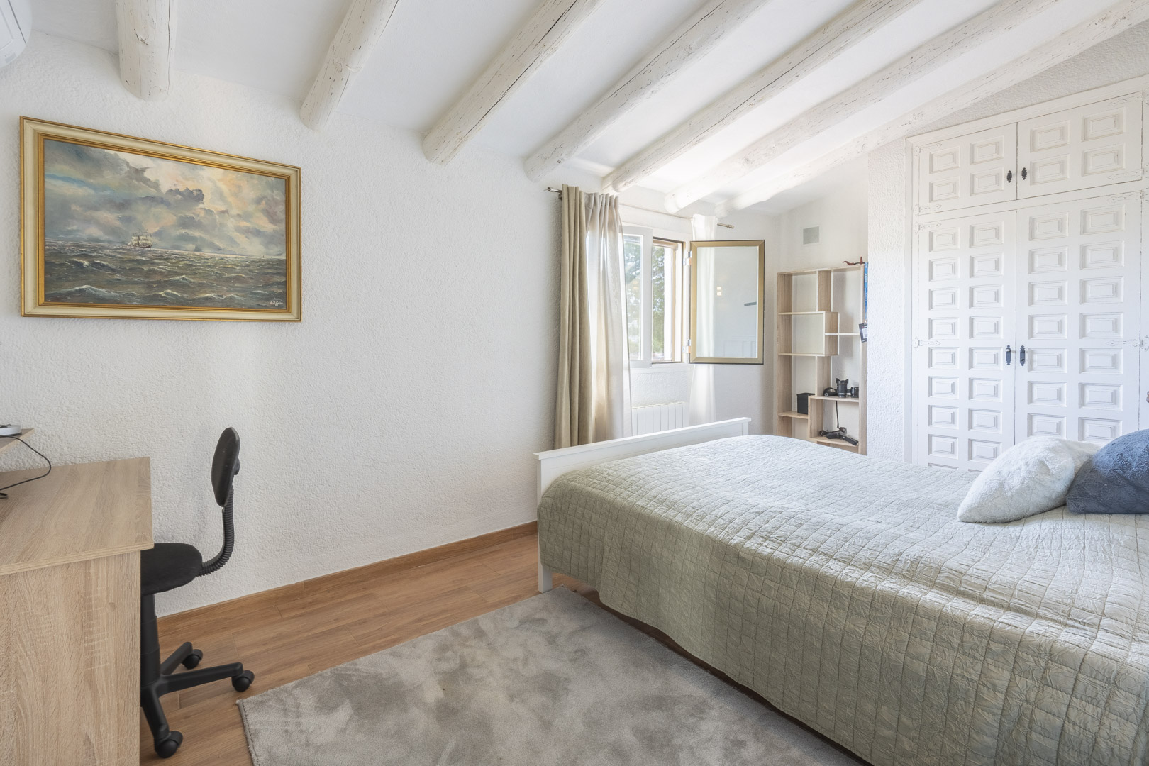 Chambre avec poutres apparentes peintes en blanc, plafonds mansardés, placards intégrés de style traditionnel et coin bureau lumineux.