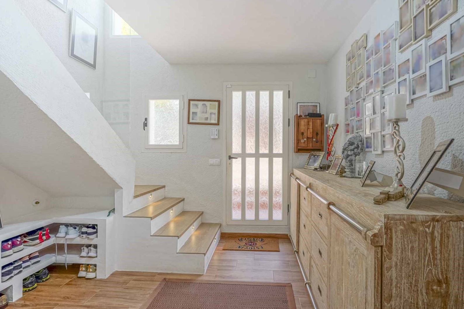 Hall d'entrée lumineux avec escalier en bois et éclairage LED intégré, buffet en bois rustique et rangement optimisé sous l'escalier.