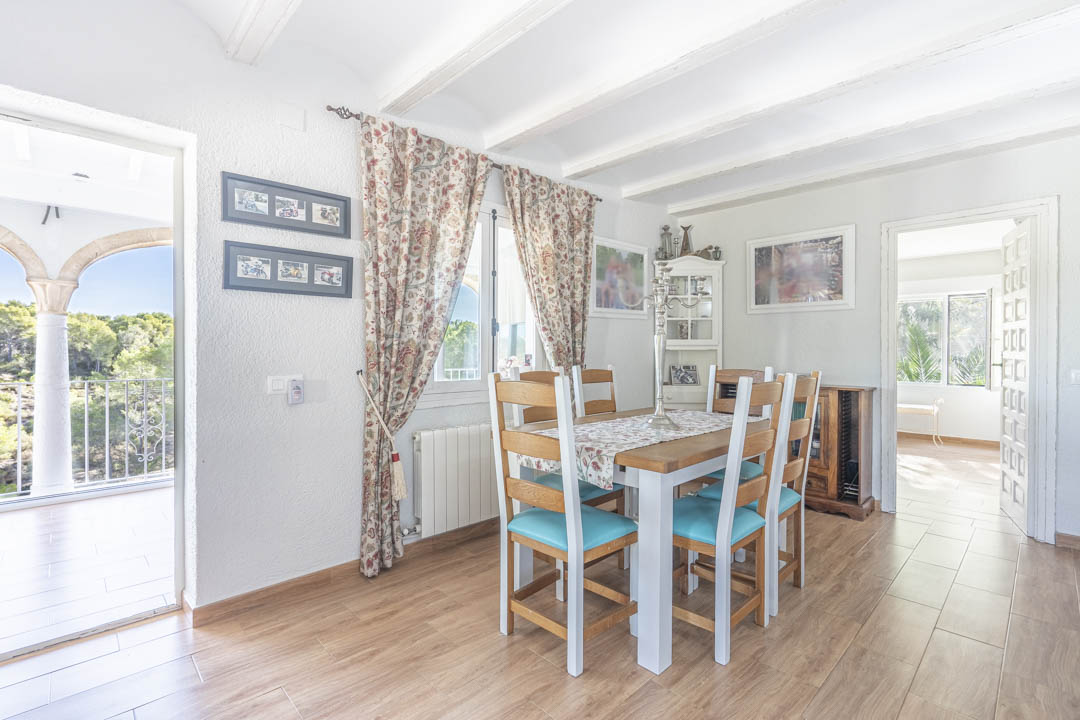Salle à manger lumineuse avec plafond à poutres blanches, sol imitation bois et accès direct à une naya offrant une vue sur la pinède environnante.