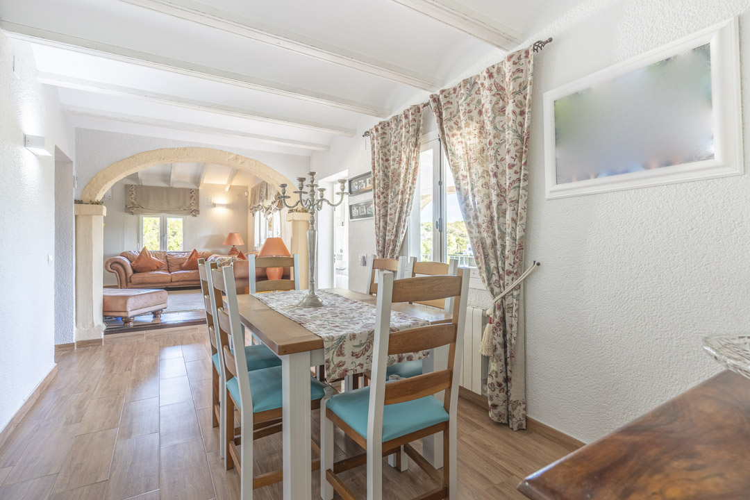 Salle à manger lumineuse avec poutres blanches et arche en pierre de Tosca. Le sol en grès cérame imitation bois complète le mobilier rustique.