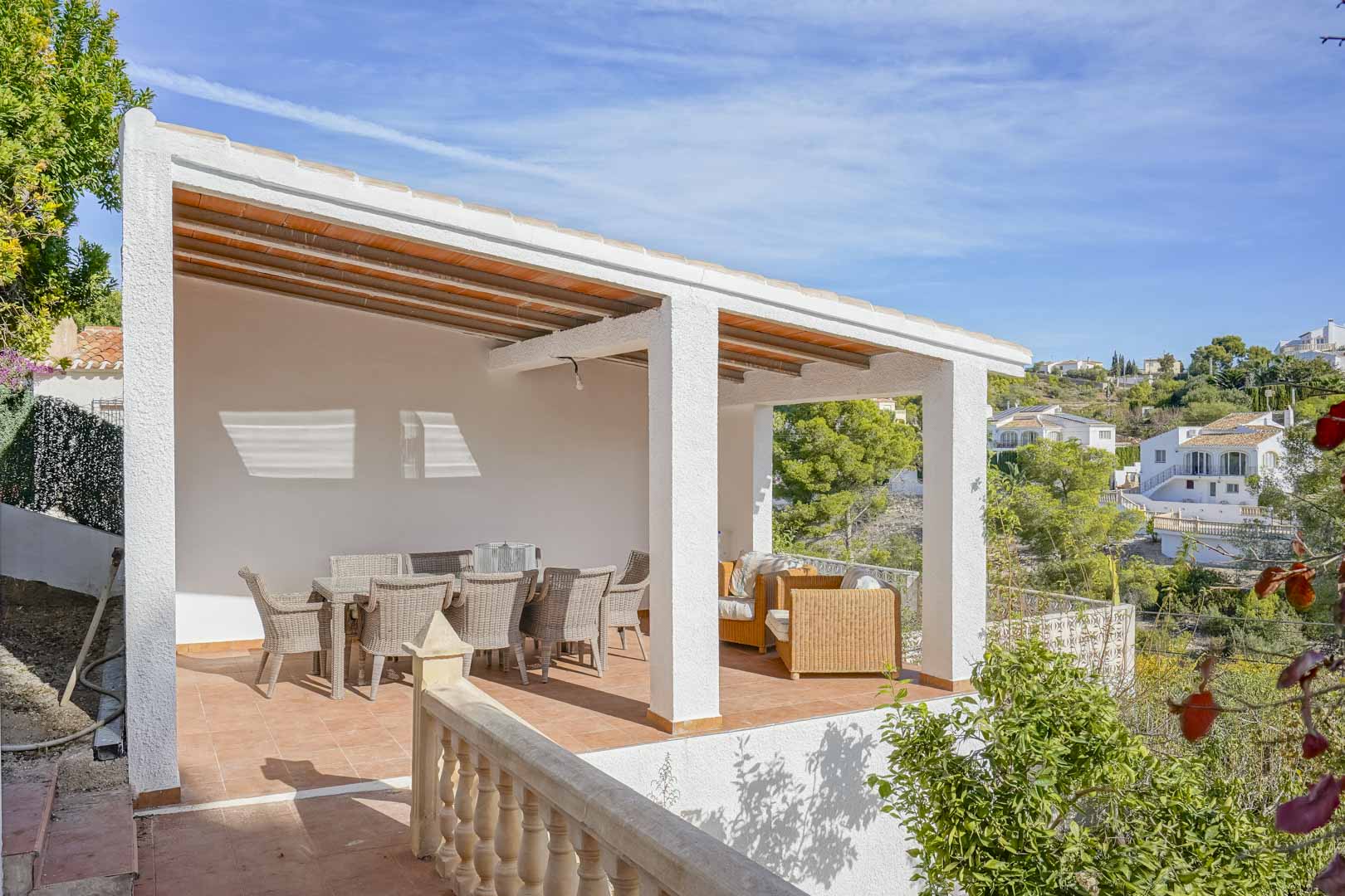 Terrasse couverte avec plafond à poutres apparentes, mobilier en osier et vue dégagée sur la vallée et la végétation environnante.