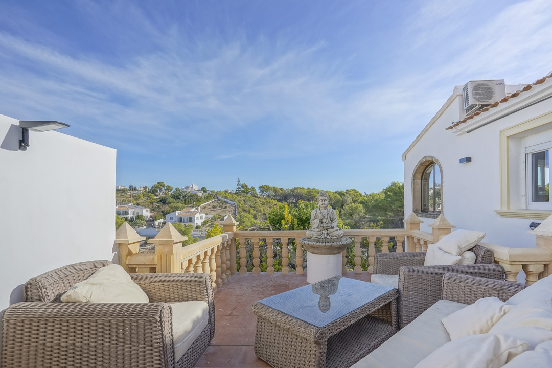 Terrasse surélevée avec mobilier en rotin, balustrade en pierre traditionnelle et vue dégagée sur les collines environnantes et les villas de Jávea.