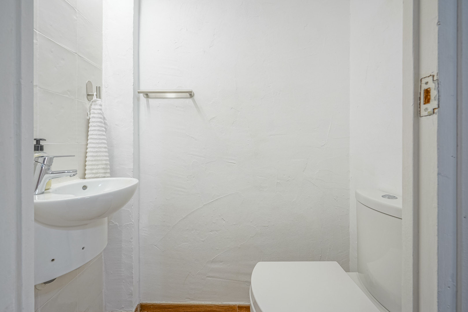 Toilettes d'invités compactes avec murs blancs texturés, lavabo suspendu en céramique et robinetterie chromée. Comprend un porte-serviettes en acier.