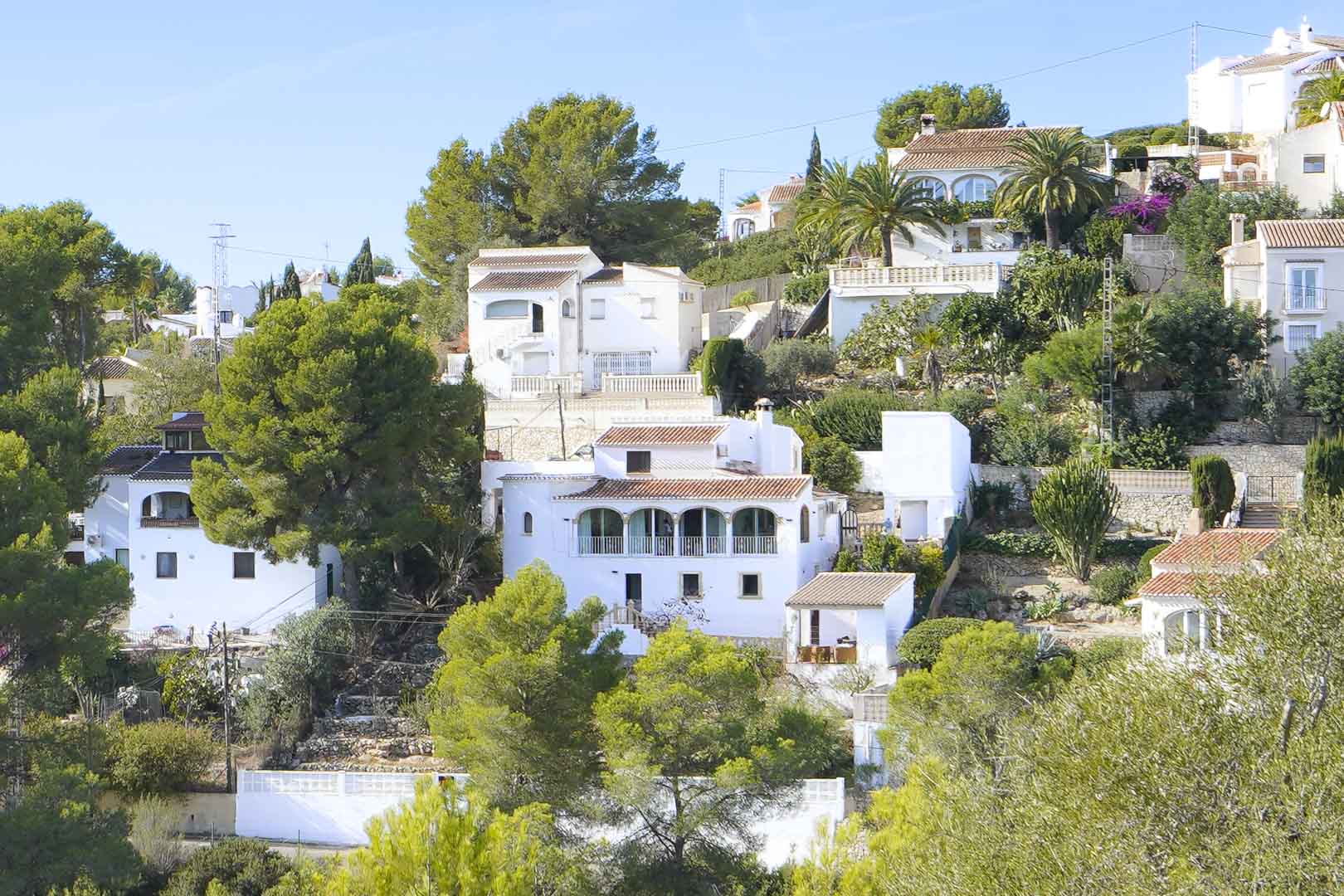 Vue extérieure de la villa à plusieurs niveaux avec sa naya à arches traditionnelle, ses façades blanches et son environnement verdoyant de pins à Jávea.