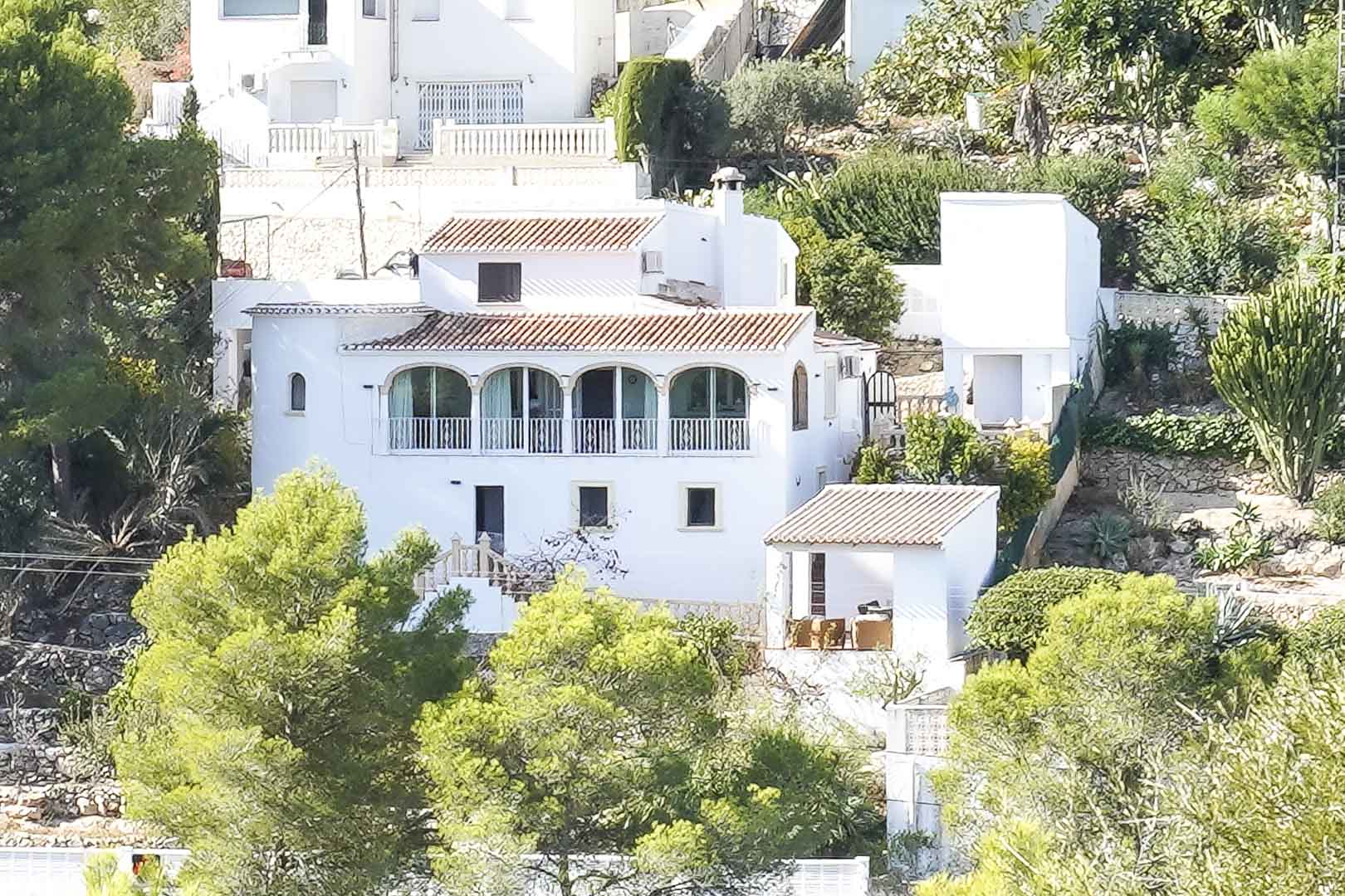 Vue extérieure de la villa blanche avec toitures en tuiles et naya à arches, intégrée dans un terrain en pente entouré de pins méditerranéens.