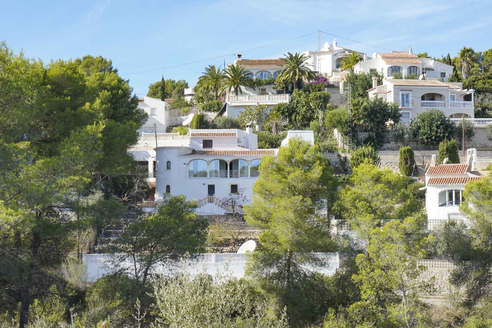 Vue extérieure de la villa méditerranéenne sur une colline boisée, avec sa façade blanche, sa naya vitrée et sa tour circulaire traditionnelle.