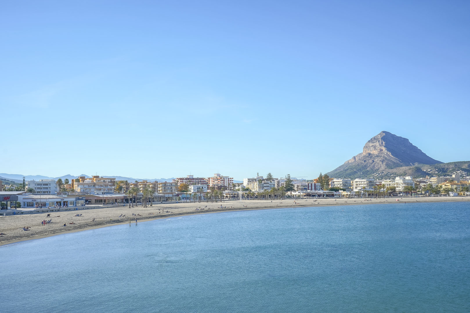Vue panoramique de la plage de l'Arenal à Jávea, avec sa baie de sable fin et la silhouette du Montgó en arrière-plan.