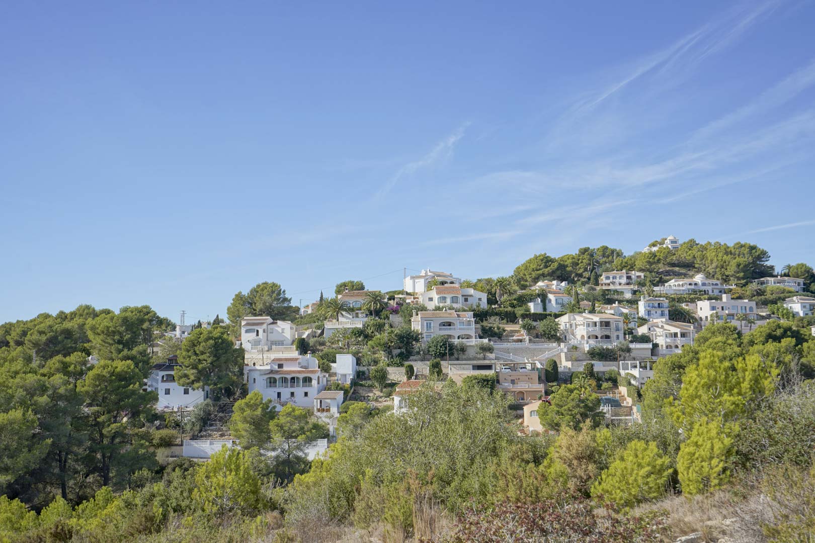 Vue panoramique du quartier résidentiel de Pinomar à Jávea, avec des villas traditionnelles nichées sur une colline verdoyante sous un ciel bleu.