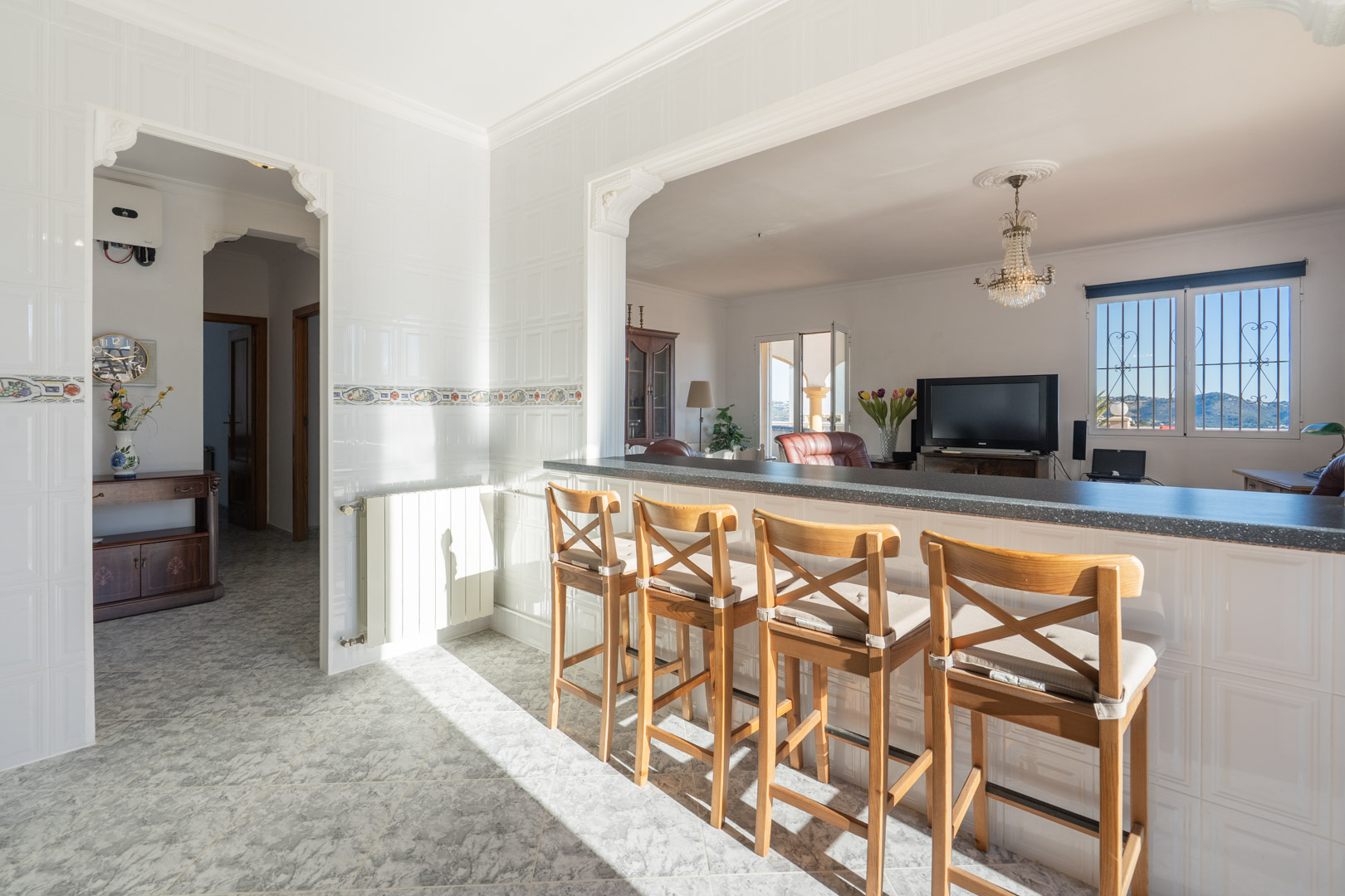 Bar de cuisine avec tabourets en bois ouvert sur le salon, avec murs carrelés blancs, arches classiques et vue sur les montagnes depuis la fenêtre.