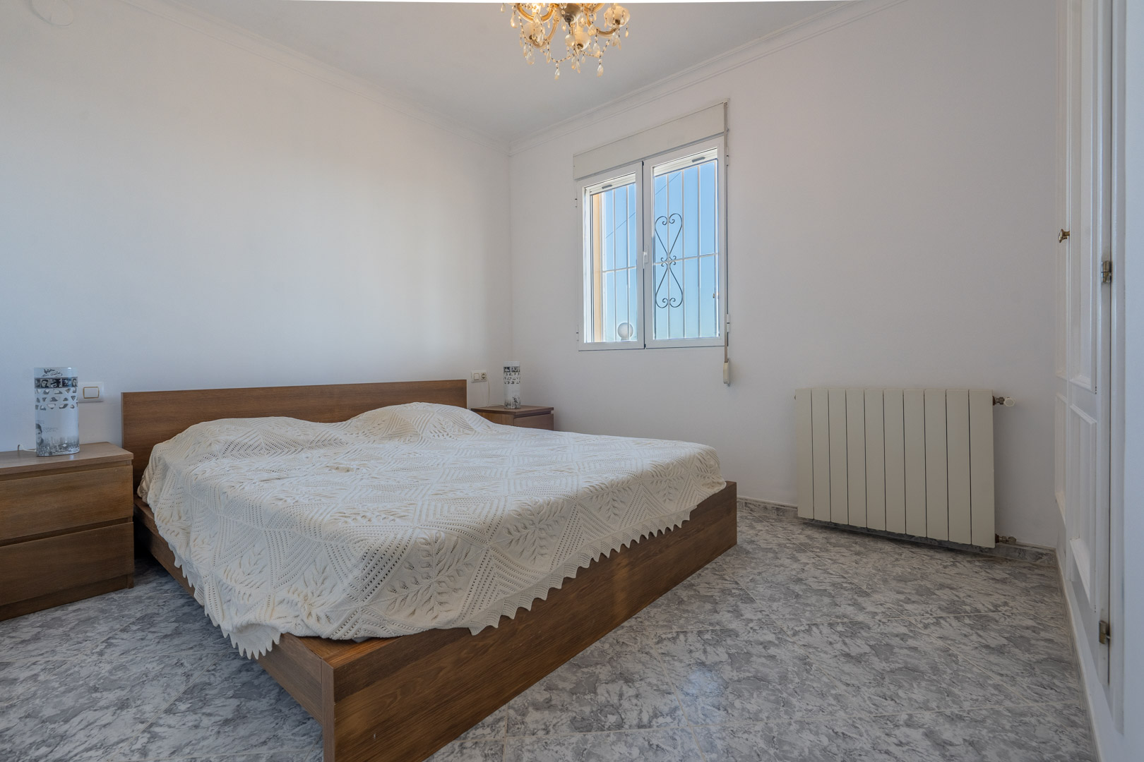 Chambre lumineuse avec sol en grès effet marbre, lit en bois et tables de chevet assorties, placards intégrés blancs et chauffage central par radiateur.