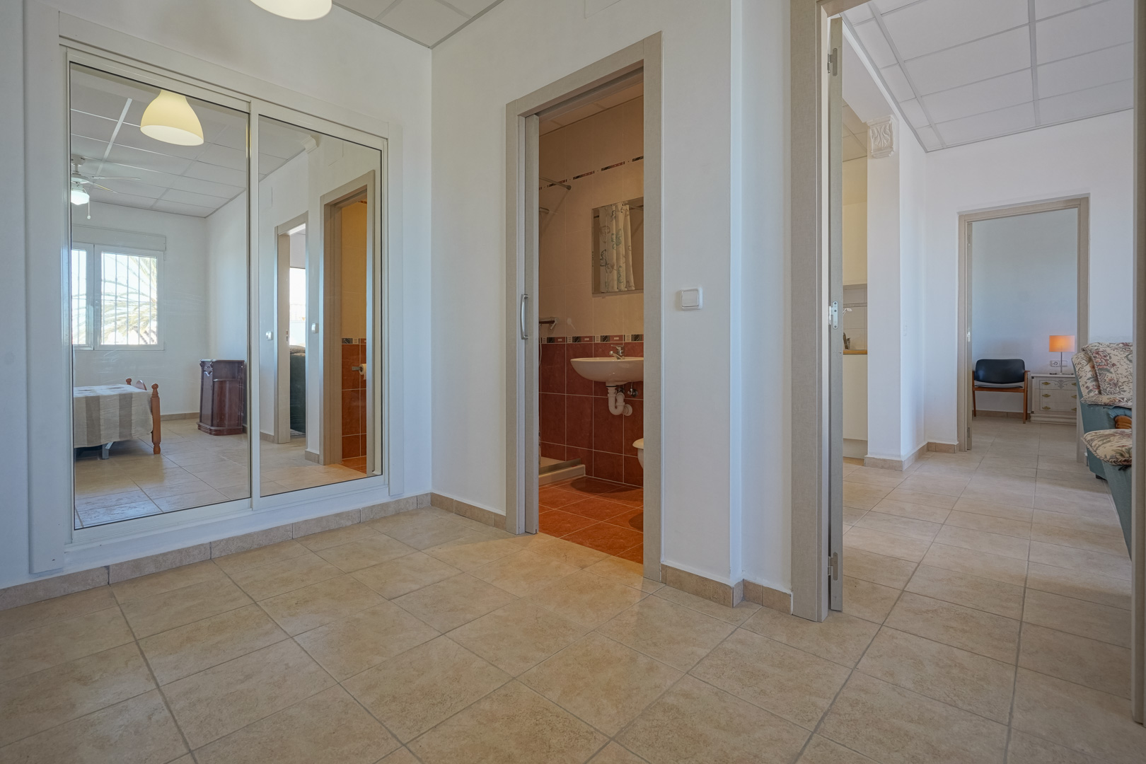 Couloir de distribution avec sol en grès, grand placard à portes coulissantes miroitantes et accès direct à une salle de bain carrelée et aux chambres.