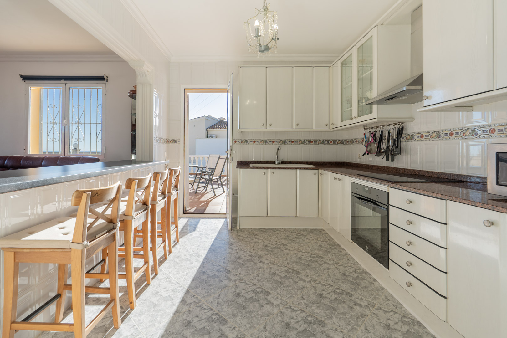 Cuisine semi-ouverte avec placards blancs, plans de travail en granit et bar. Elle dispose d'un accès direct à la terrasse et d'un sol en grès cérame.