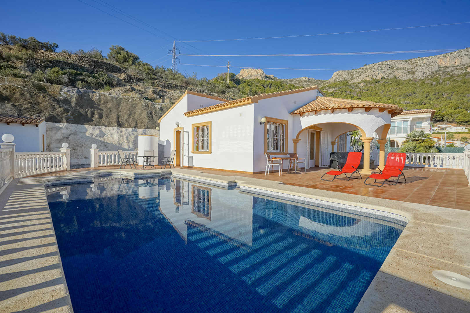 Extérieur de la villa avec piscine privée, terrasse en terre cuite et porche voûté, offrant une vue sur les formations rocheuses de la Sierra de Oltà.