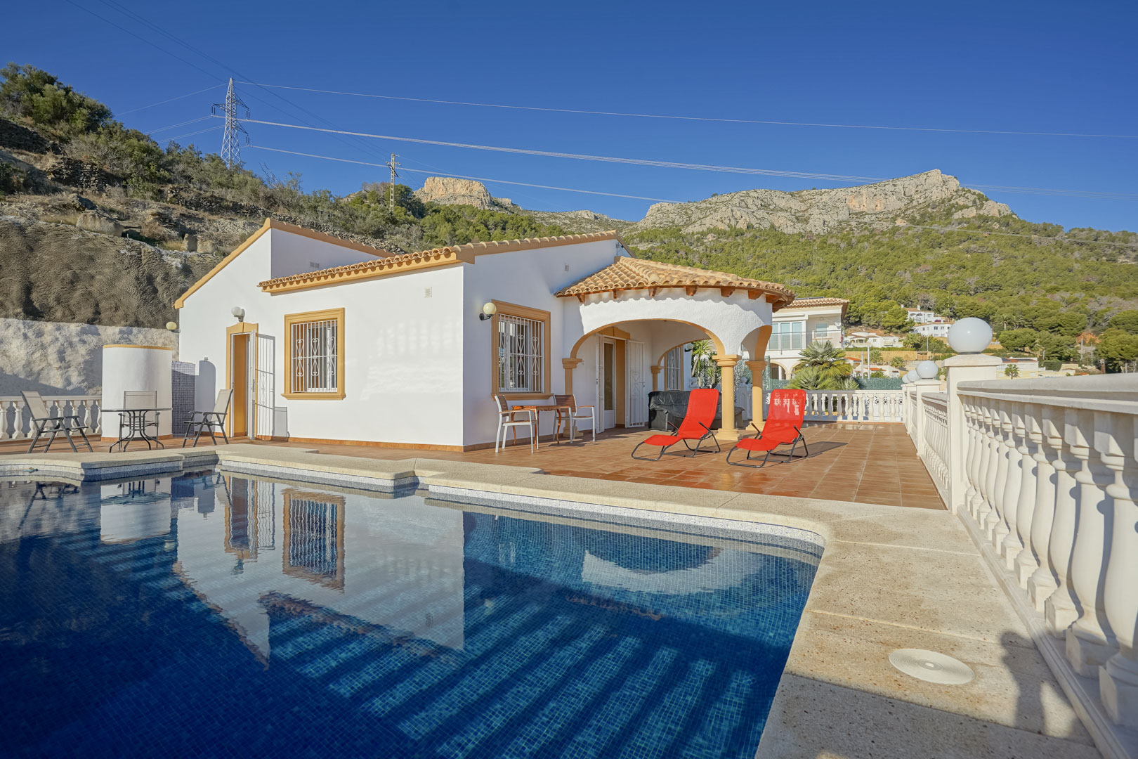 Extérieur de la villa avec piscine privée, terrasse en terre cuite et porche voûté traditionnel, offrant une vue directe sur les montagnes de la Sierra de Oltà.