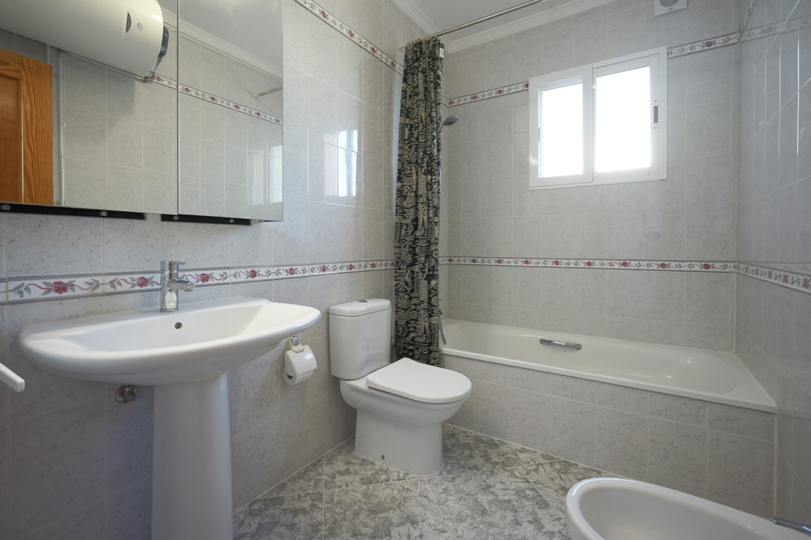 Salle de bains traditionnelle avec murs carrelés à motifs floraux, comprenant une baignoire, un lavabo sur colonne et une armoire à miroir.