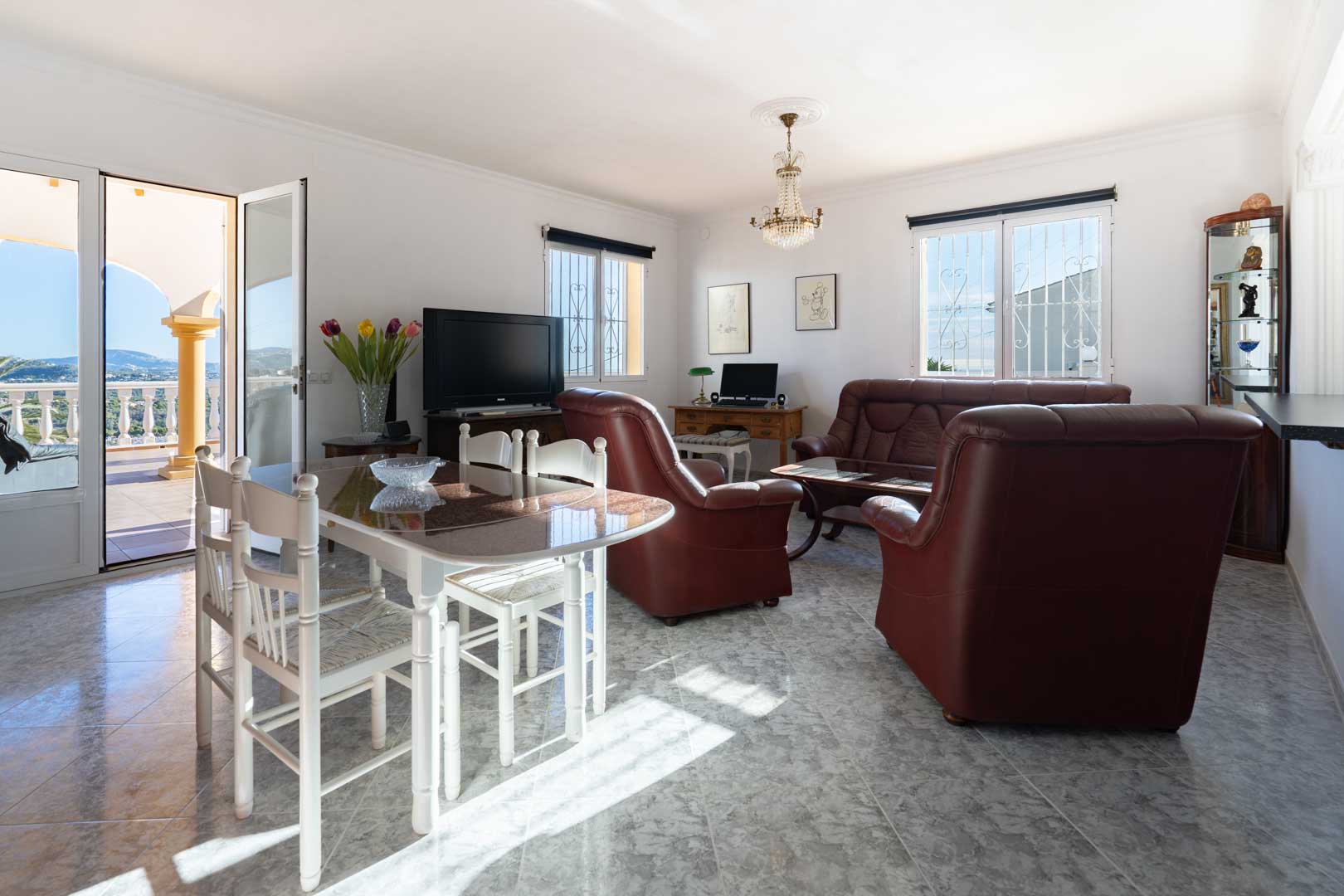 Salon-salle à manger lumineux avec carrelage effet marbre, canapés en cuir et accès direct à une terrasse offrant une vue dégagée sur la mer.