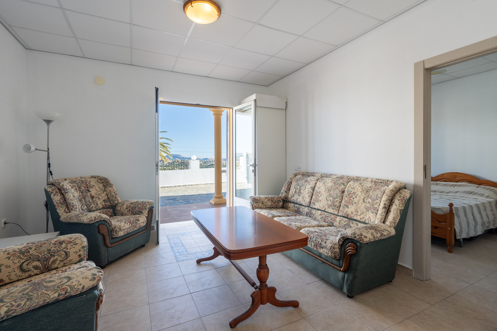 Séjour de l'appartement d'invités avec canapés à motifs floraux, table basse en bois et accès direct à la terrasse carrelée.