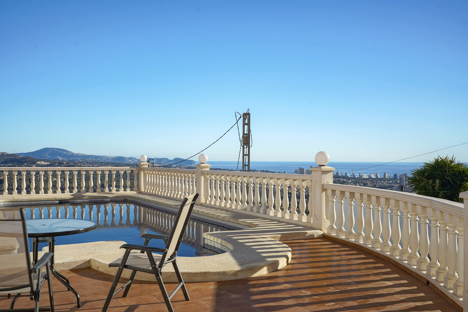 Terrasse avec piscine et balustrade classique offrant une vue panoramique sur la mer Méditerranée et la silhouette urbaine de Calpe.