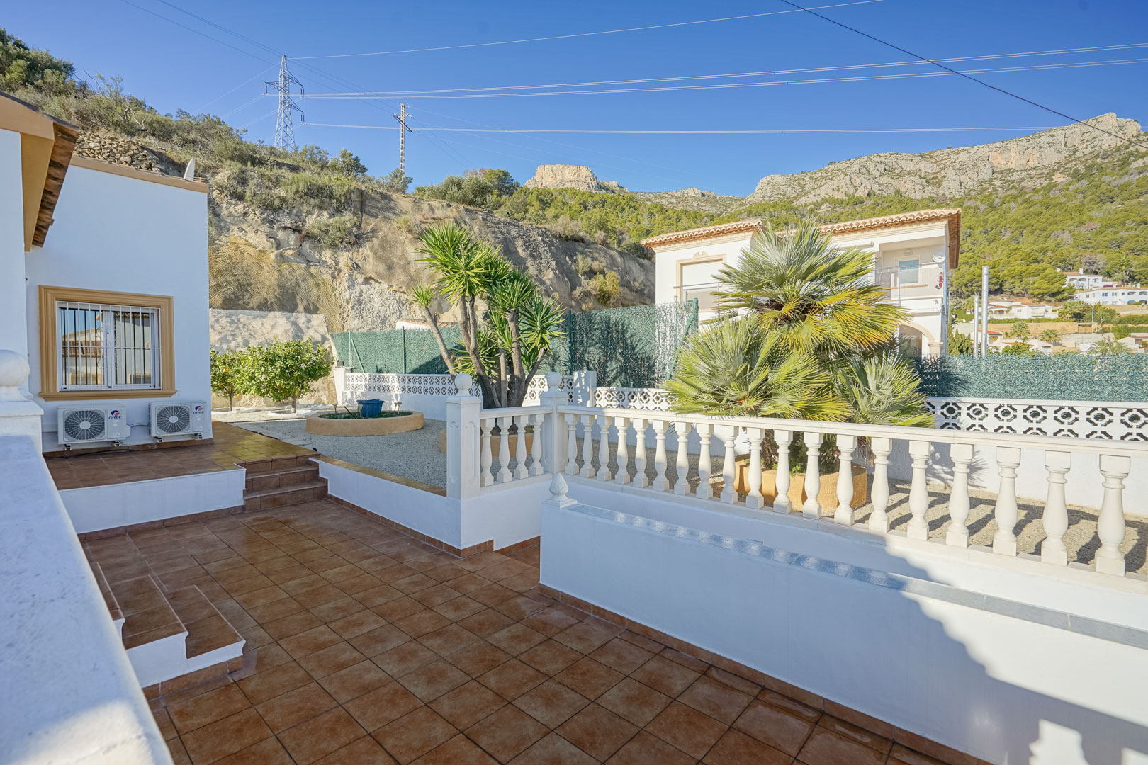 Terrasse extérieure avec carrelage rustique et balustrade blanche, bordée d'un jardin méditerranéen et offrant une vue sur les parois de la Sierra de Oltà.
