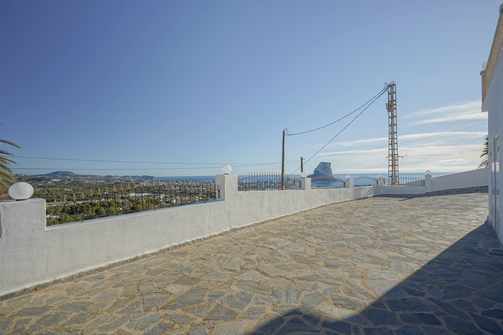 Terrasse pavée en pierre naturelle offrant une vue panoramique sur la mer Méditerranée et le Peñón de Ifach, bordée d'un muret blanc avec ferronnerie.