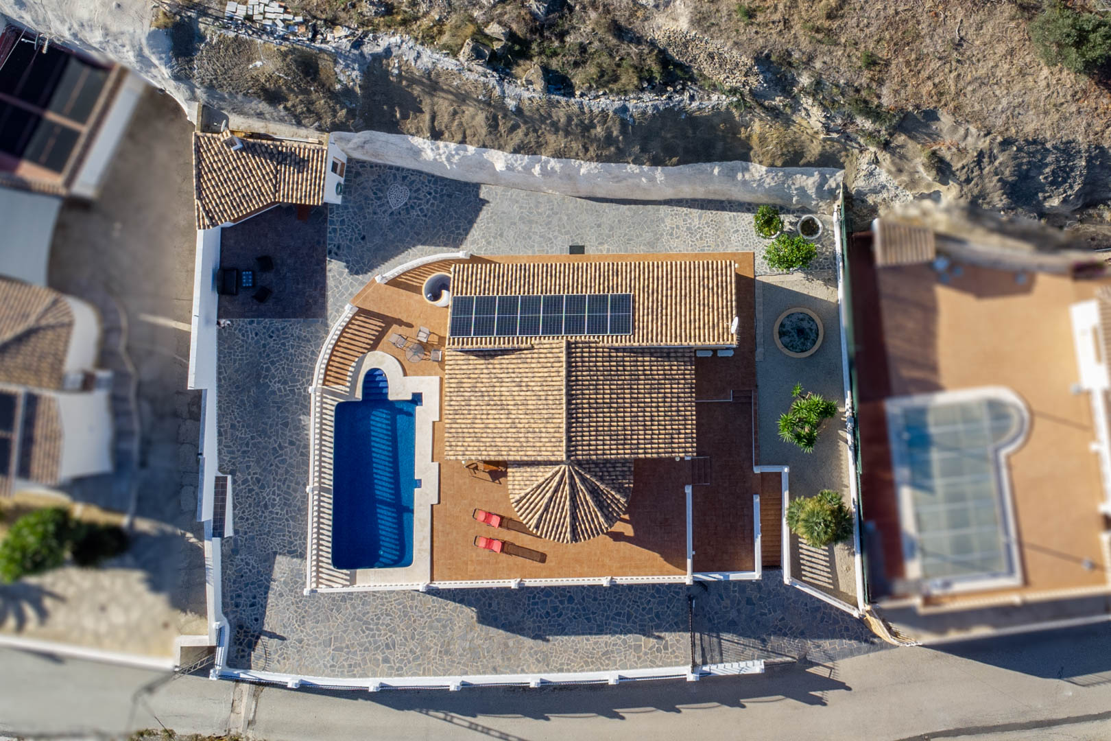 Vue aérienne montrant la toiture en tuiles équipée de panneaux solaires, la piscine privée et les vastes terrasses en pierre et terre cuite.