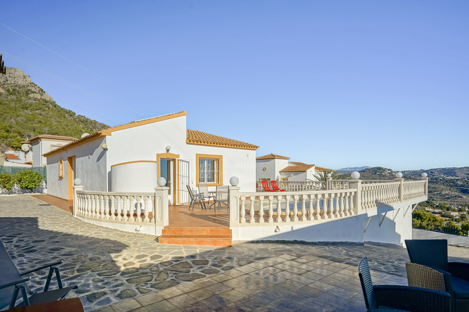 Vue extérieure de la villa avec une grande terrasse en terre cuite, balustrade classique et vues panoramiques sur la côte et la Sierra de Oltà.