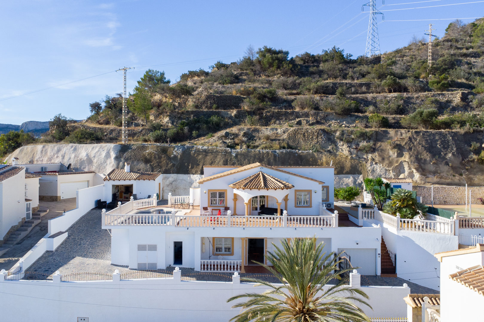 Vue extérieure de la villa blanche sur deux niveaux avec terrasses à balustrades, piscine privée et cuisine d'été, située au pied de la Sierra de Oltà.