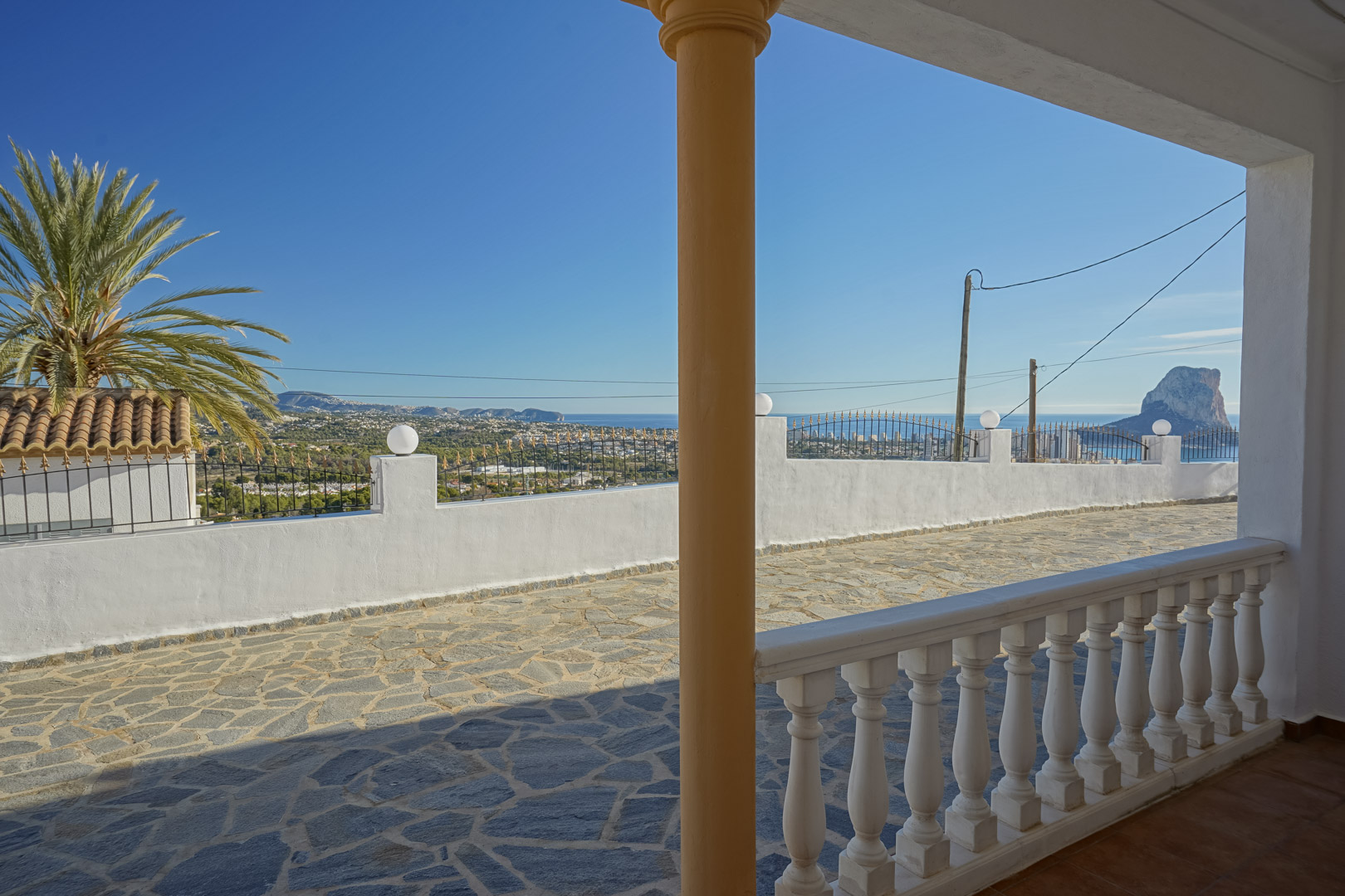 Vue panoramique depuis le porche couvert avec balustrade blanche, surplombant la terrasse en pierre et le célèbre Peñón de Ifach à Calpe.