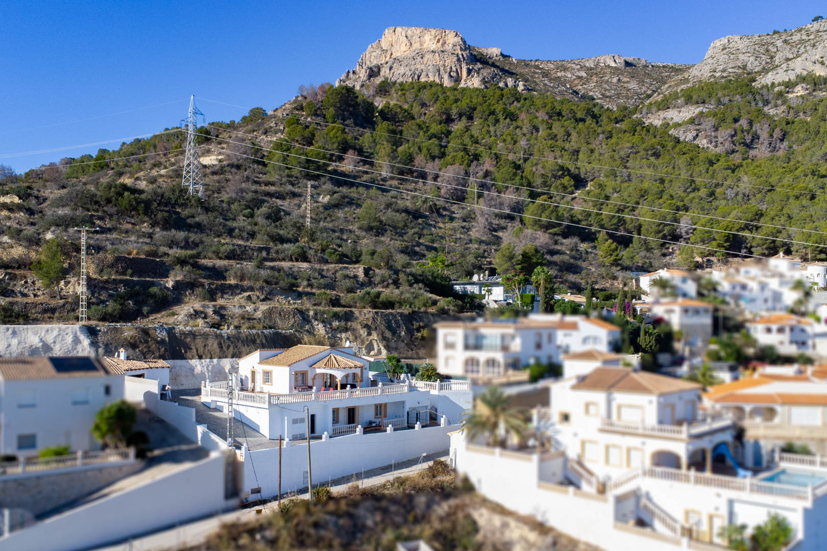 Vue surélevée de la villa blanche au pied de la Sierra de Oltà, illustrant son architecture traditionnelle avec toits en tuiles et terrasses spacieuses.