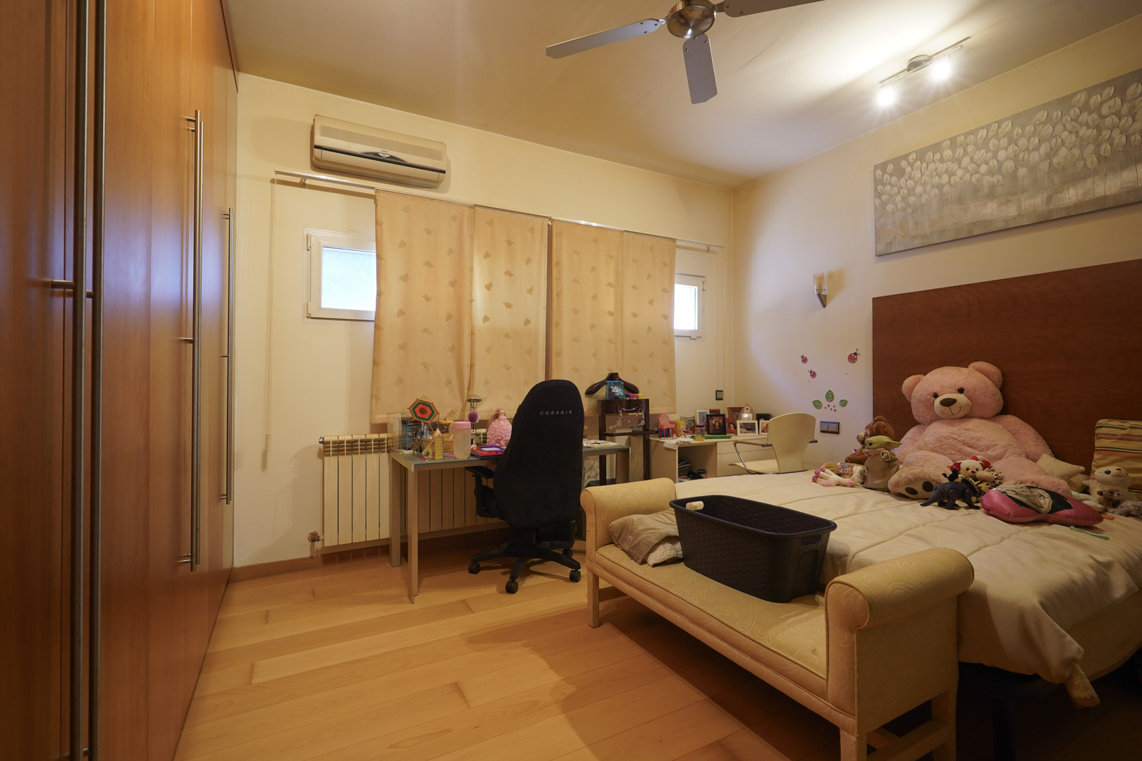 Chambre avec parquet en bois noble, grands placards intégrés en bois, coin bureau, climatisation et ventilateur de plafond.