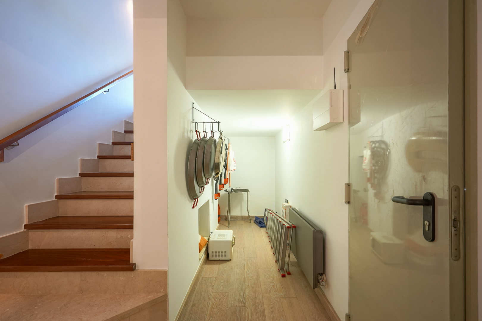 Couloir de service avec rangement pour ustensiles de cuisine, jouxtant un escalier élégant en pierre et bois avec main courante.