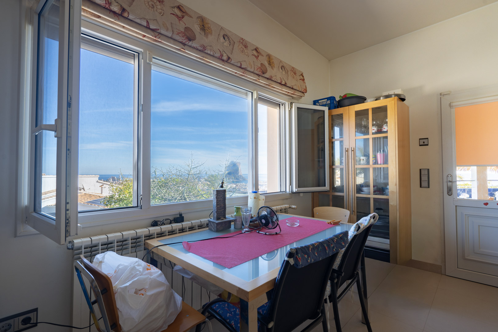 Espace repas doté d'une grande fenêtre avec vue sur le Peñón de Ifach. Comprend une table en bois avec plateau en verre et un buffet vitré classique.