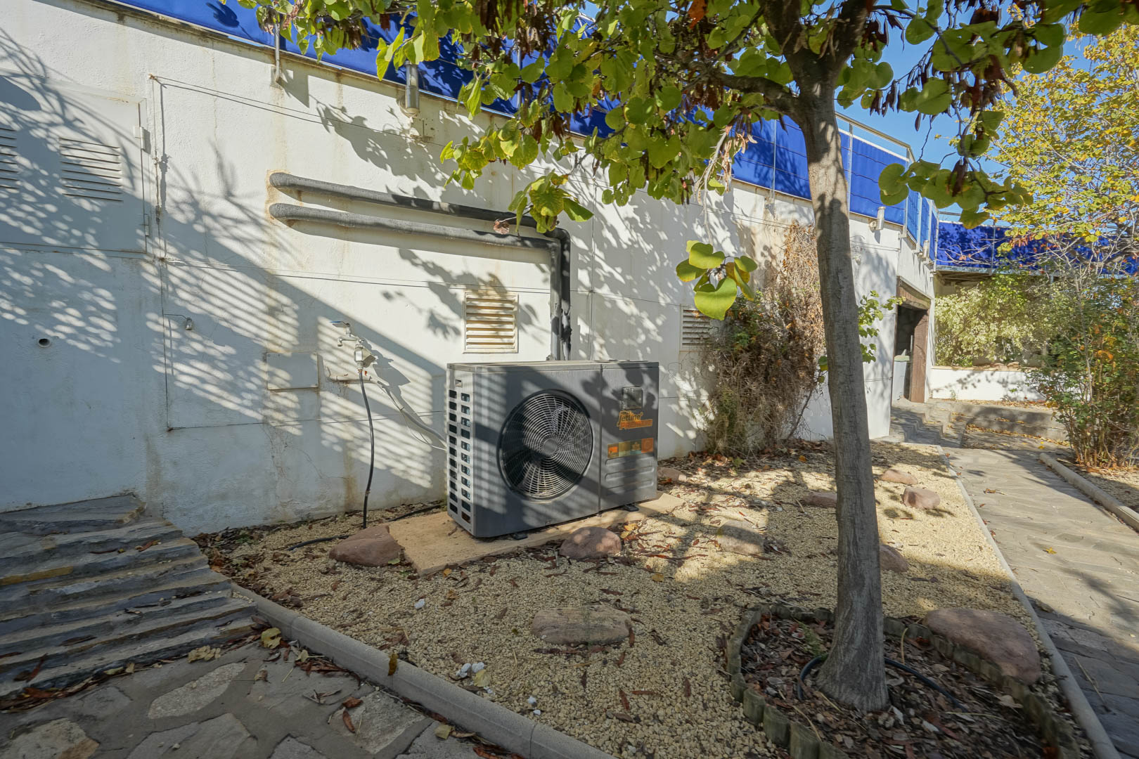Espace technique extérieur comprenant une pompe à chaleur Jetline Premium installée sur gravier, à côté des conduites murales et du jardin.