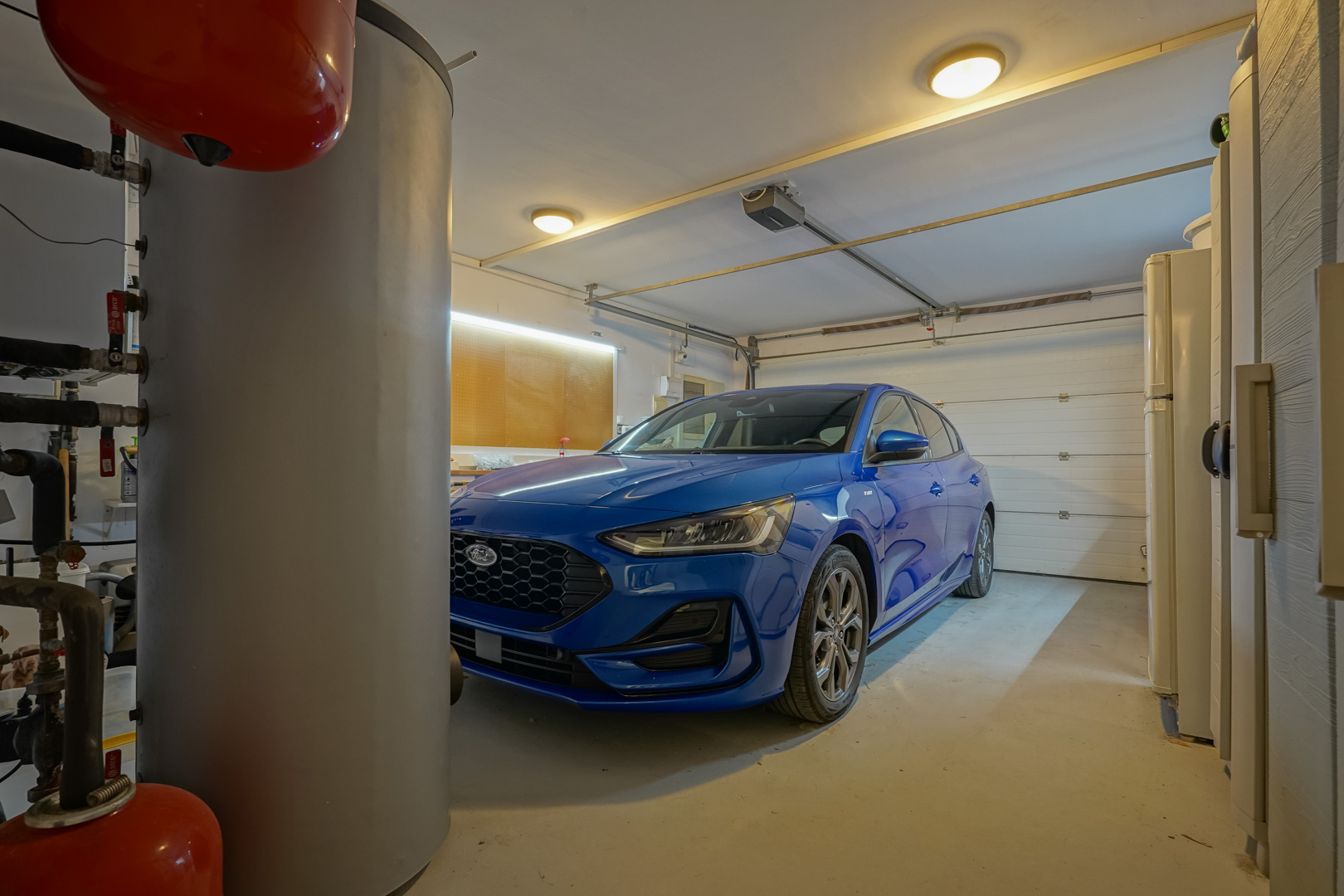 Garage privé avec porte automatique, espace atelier éclairé par LED et installations techniques comprenant un ballon d'eau chaude.