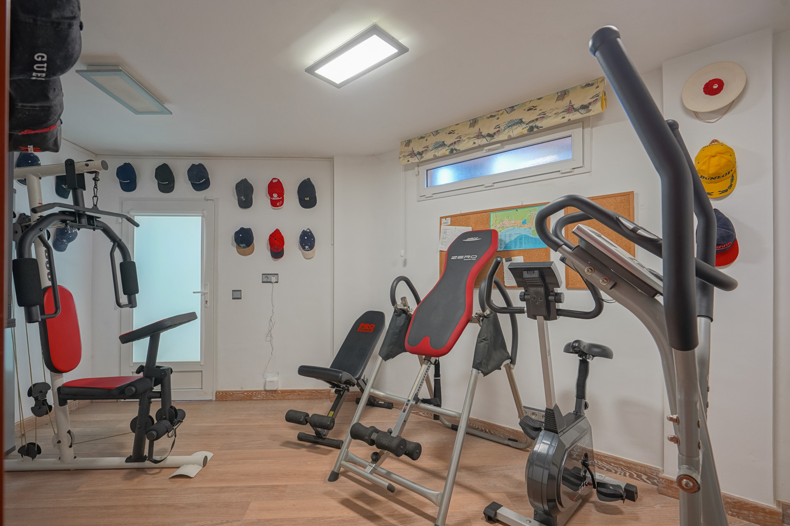 Salle de sport privée avec parquet, équipée d'une machine multifonction, d'un vélo d'appartement et d'une table d'inversion sous éclairage LED.