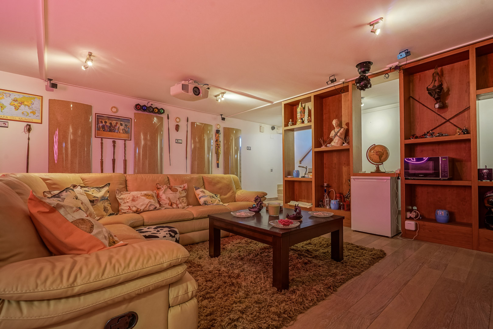 Salle multimédia équipée d'un canapé d'angle en cuir, d'un projecteur au plafond, de jeux de lumières et d'un meuble de rangement en bois avec minibar.