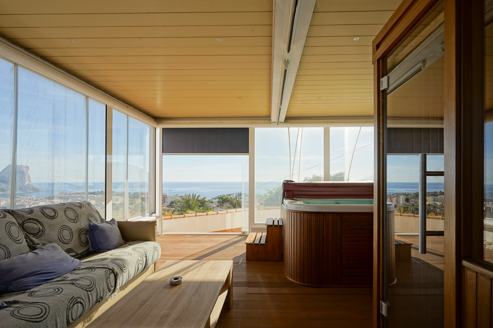 Terrasse vitrée avec jacuzzi habillé de bois, coin salon et vue panoramique sur le Peñón de Ifach. Dispose de parquet au sol et d'un plafond avec éclairage encastré.