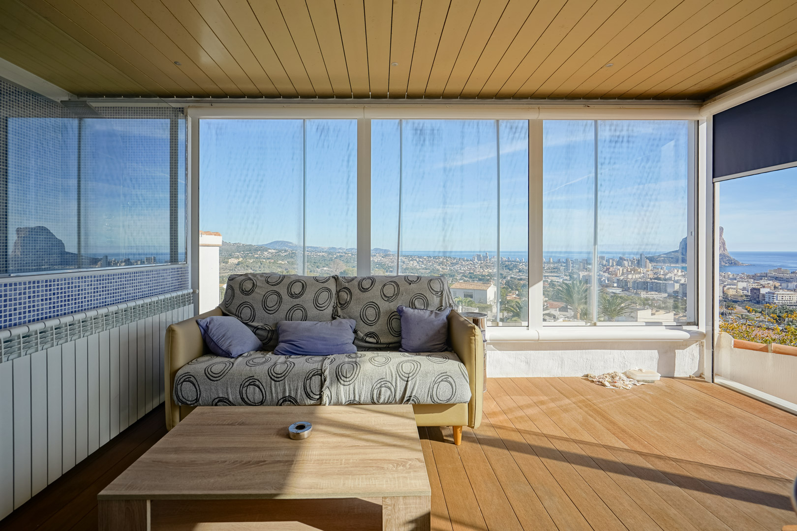 Terrasse vitrée avec rideaux de verre, parquet au sol et vue panoramique sur Calpe et le Peñón de Ifach. Comprend un plafond lambrissé et un coin salon lumineux.