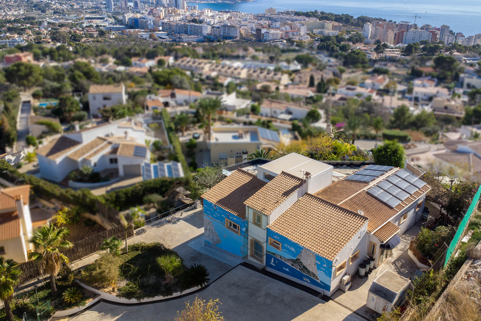 Vue aérienne de la villa avec fresques murales, toiture en tuiles et panneaux solaires, surplombant le littoral et la ligne d'horizon de Calpe.