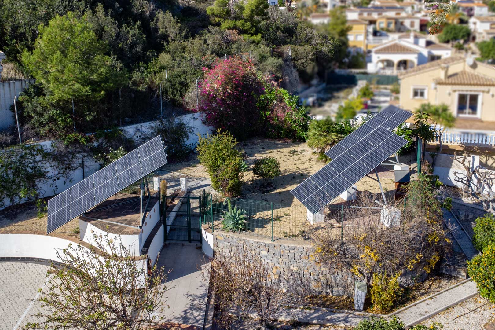Vue aérienne du système photovoltaïque comprenant trois tours solaires motorisées, intégrées dans le jardin avec des murs en pierre et une végétation locale.