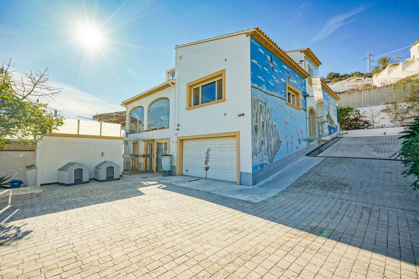 Vue extérieure avec une large allée pavée, un garage intégré et une peinture murale artistique représentant un paysage marin sur la façade latérale.