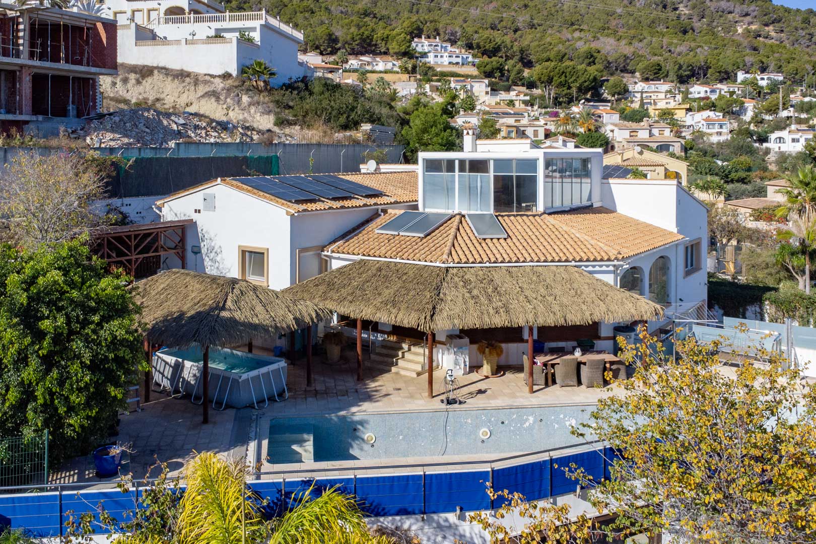Vue extérieure de la villa avec panneaux solaires, terrasses abritées par des pergolas en brande, piscine et solarium vitré au niveau supérieur à Calpe.