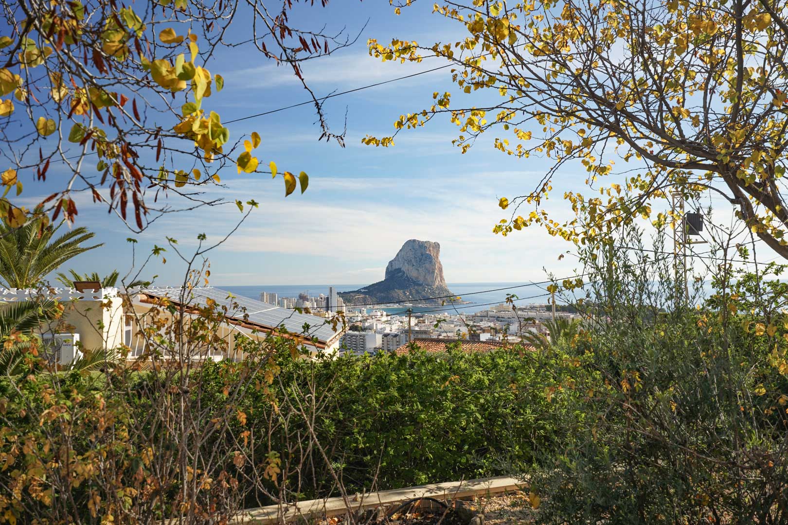 Vue panoramique sur le Peñón de Ifach et Calpe depuis la propriété, mettant en avant le système de panneaux solaires en toiture au milieu d'une végétation variée.