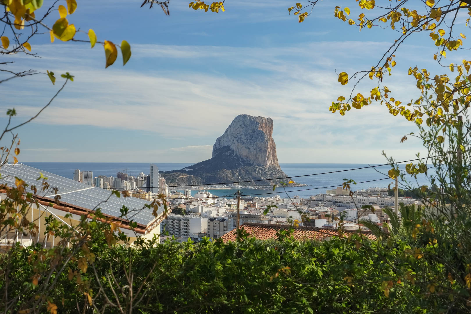 Vue panoramique sur le Peñón de Ifach et la skyline de Calpe, mettant en avant les panneaux solaires sur le toit au milieu d'un cadre verdoyant.