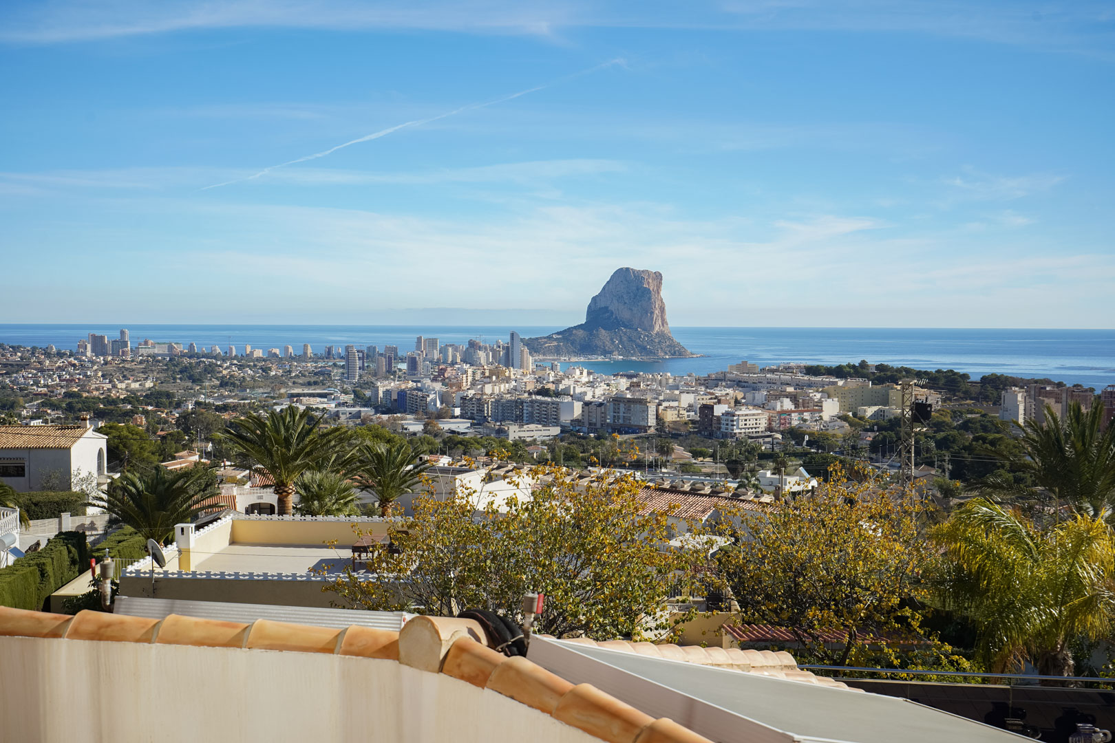 Vue panoramique sur le rocher d'Ifach et la silhouette urbaine de Calpe depuis la terrasse, surplombant la mer Méditerranée et les jardins environnants.